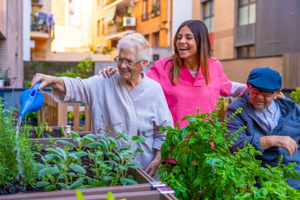 Participants watering herbs in a raised garden bed with a caregiver